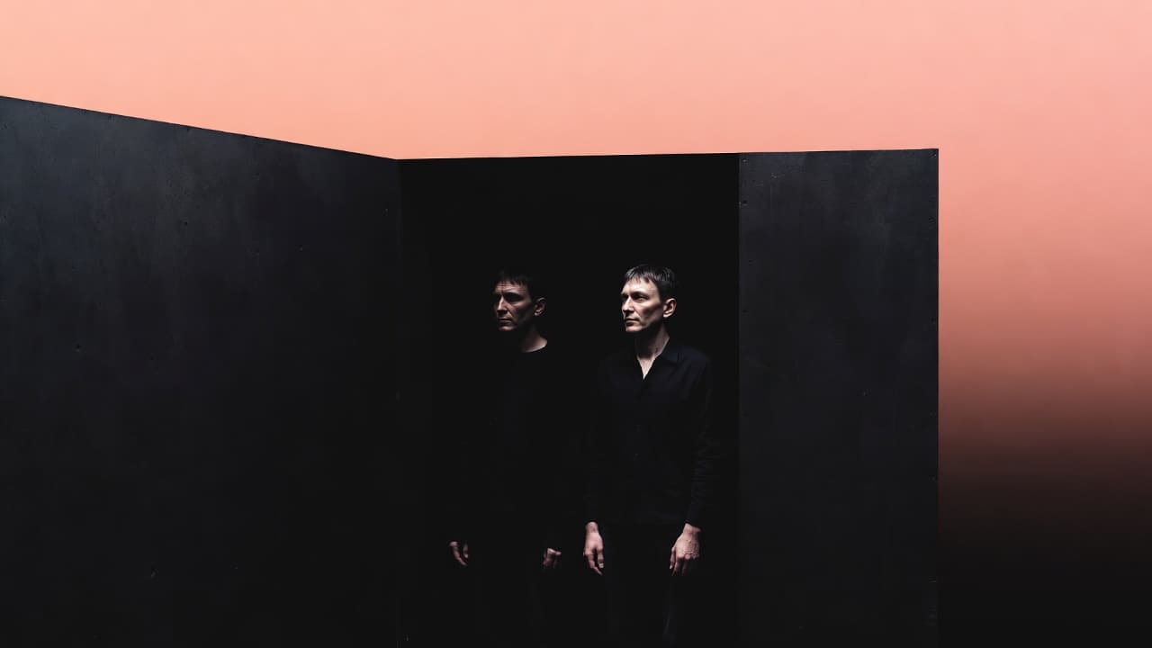 Two figures in a dark geometric space against a warm coral background - evoking the concept of Clones